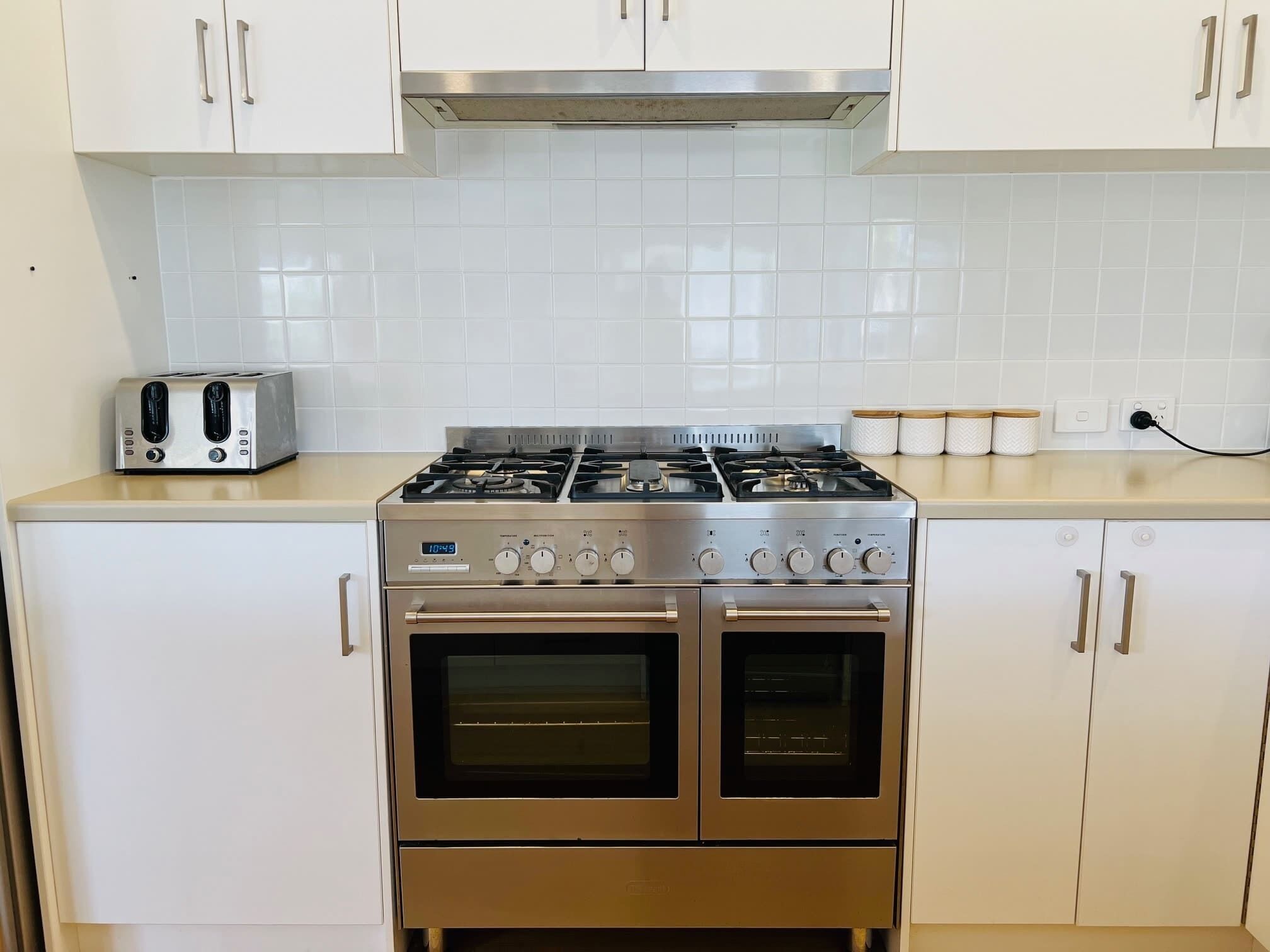 A kitchen with white cabinets, a stainless steel stove, a toaster, and a double oven.