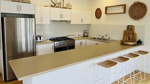 Une cuisine moderne dotée d’un réfrigérateur en acier inoxydable, d’une cuisinière à gaz, de meubles blancs et d’un coin bar avec des tabourets.