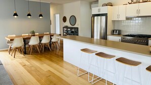 Une cuisine moderne avec une table à manger en bois, des tabourets de bar blancs, un réfrigérateur en acier inoxydable et une cuisinière à gaz.