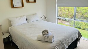 Une chambre à coucher avec un lit, des oreillers, une table de chevet, une lampe et une fenêtre donnant sur un paysage verdoyant.