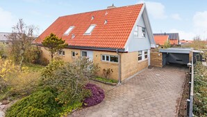 Une maison à deux étages, avec un toit recouvert de tuiles rouges, une façade en briques et une allée pavée.