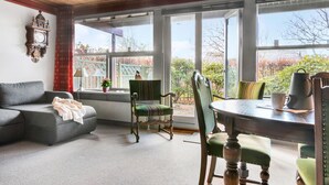 Une pièce confortable avec un canapé, un fauteuil, une table avec une tasse et une vue sur le jardin grâce à de grandes fenêtres.