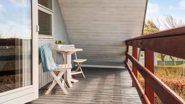 Une terrasse en bois avec une table et des chaises, un pot de fleurs et une vue sur le paysage environnant.
