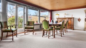 Un coin repas avec des chaises et une table en bois, de grandes fenêtres donnant sur les arbres et un plafond en bois.