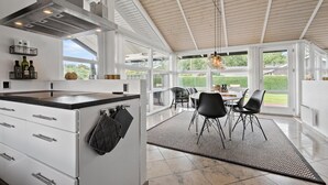 A modern kitchen with a large island, white cabinetry, and a view of the outdoors through large windows.