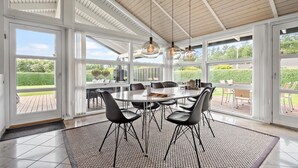 A spacious dining area with a large table and chairs, large windows offering a view of the outdoors, and pendant lighting.