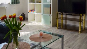 Ein Wohnzimmer mit einem Glastisch, einer Bücherwand, einem Fernseher und einer Vase mit Tulpen.