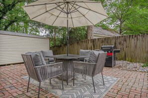 Une terrasse extérieure avec une table et des chaises, un grand parasol et un barbecue.