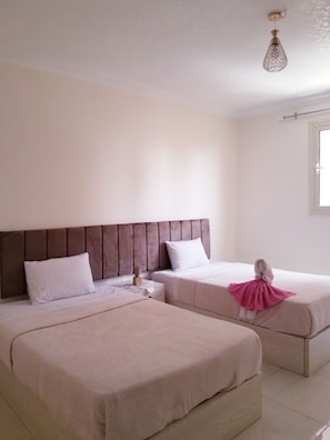 A hotel room with two beds, a headboard, a nightstand, a decorative towel, and a hanging light fixture.