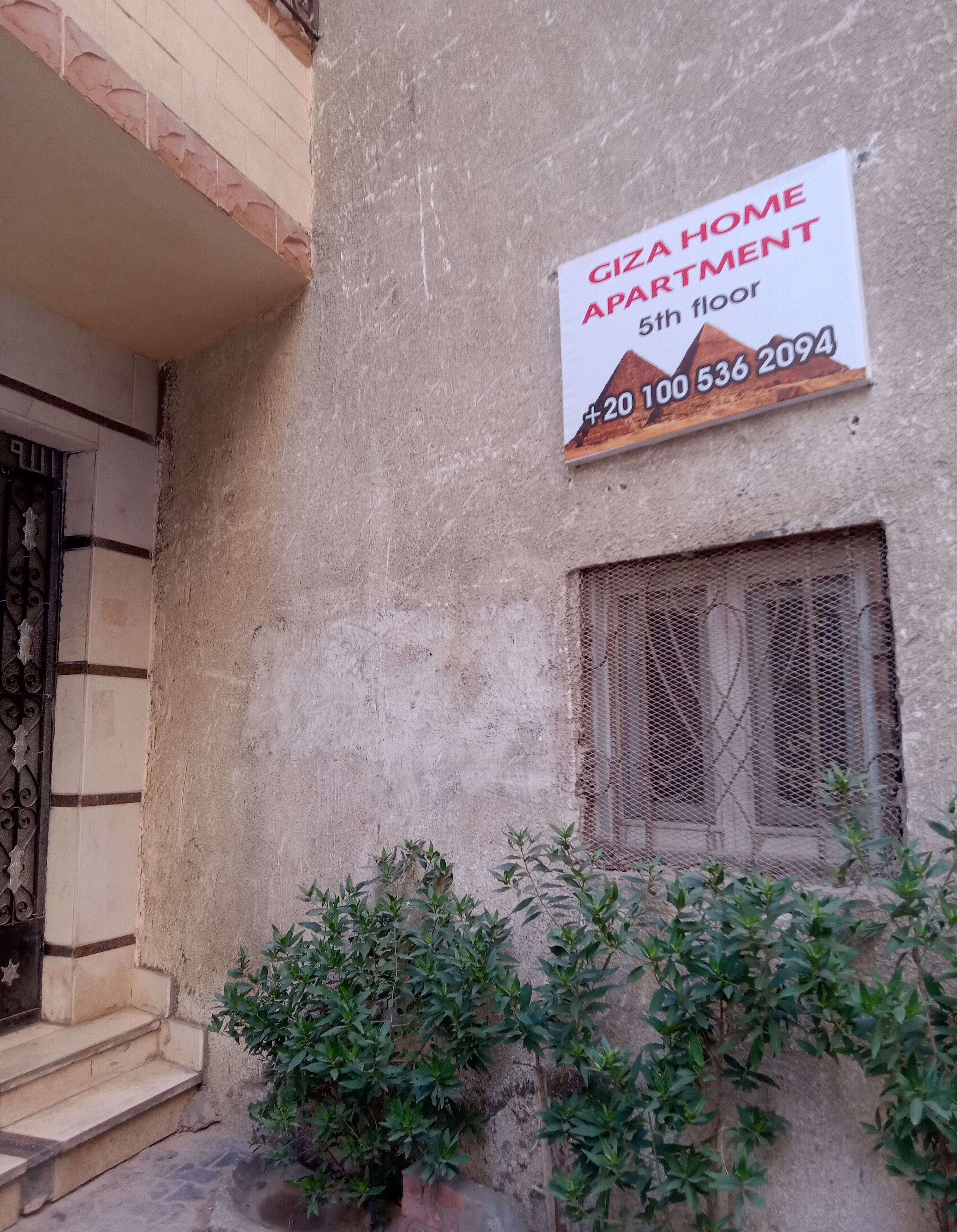 A building with a sign indicating 'GIZA HOME APARTMENT 5th floor' and a contact number.