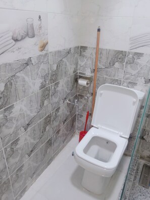 Un bagno con il water, una scopa rossa e un rotolo di carta igienica appeso al muro.