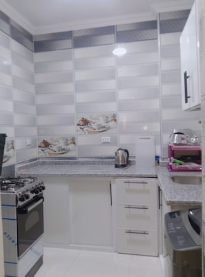 Una cucina con mobili bianchi, un fornello a gas, un forno a microonde e un lavello.