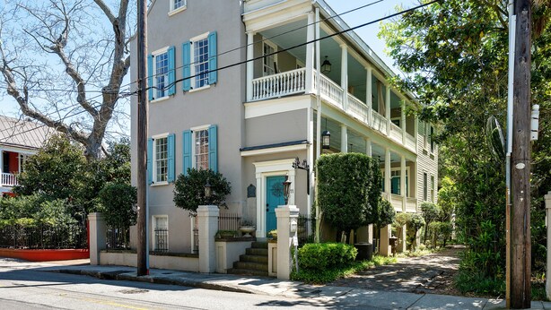 A two-story house with a balcony, a front door, and a staircase leading to the entrance. - The Heart of Historic Charleston | The Mod Suite (Charleston)