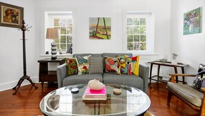 A living room with a grey sofa, colorful cushions, a glass coffee table, a lamp, and artwork on the walls. - The Heart of Historic Charleston | The Mod Suite (Charleston)