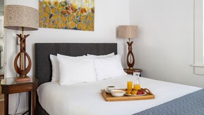 A hotel room with a large bed, a painting on the wall, a tray with breakfast items, and two lamps. - The Heart of Historic Charleston | The Mod Suite (Charleston)