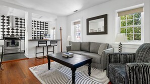 A modern living room with a sofa, armchair, coffee table, and a dining area with a kitchen in the background. - The McKenzie Suite at The Mary Scott House (Charleston)