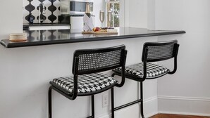 A kitchen with a black and white patterned backsplash, a white countertop, and two black metal bar stools. - The McKenzie Suite at The Mary Scott House (Charleston)