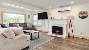 A modern living room with a fireplace, a sofa, a coffee table, and a TV mounted on the wall. - Pondview 4BR Cabin-Walk to Caverns, Hot Tub, Wi-Fi (Luray)
