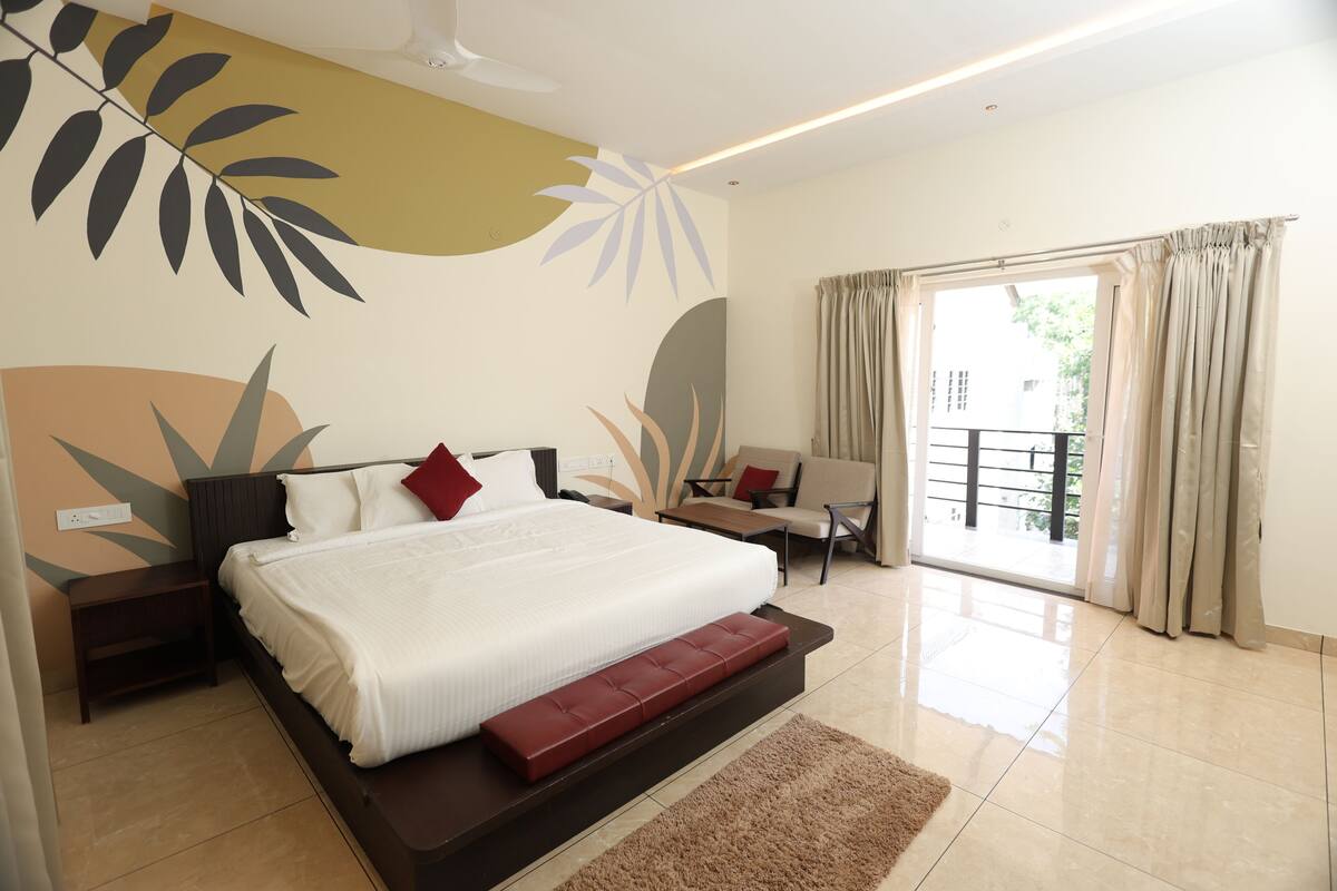 A modern hotel room with a large bed, a small desk, a sofa, and a balcony with curtains.