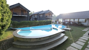 A swimming pool with a stone deck and steps leading into it, surrounded by a well-maintained lawn and a house with a balcony. - Yercaud Yellow Lake Resorrt and spa (Yercaud)