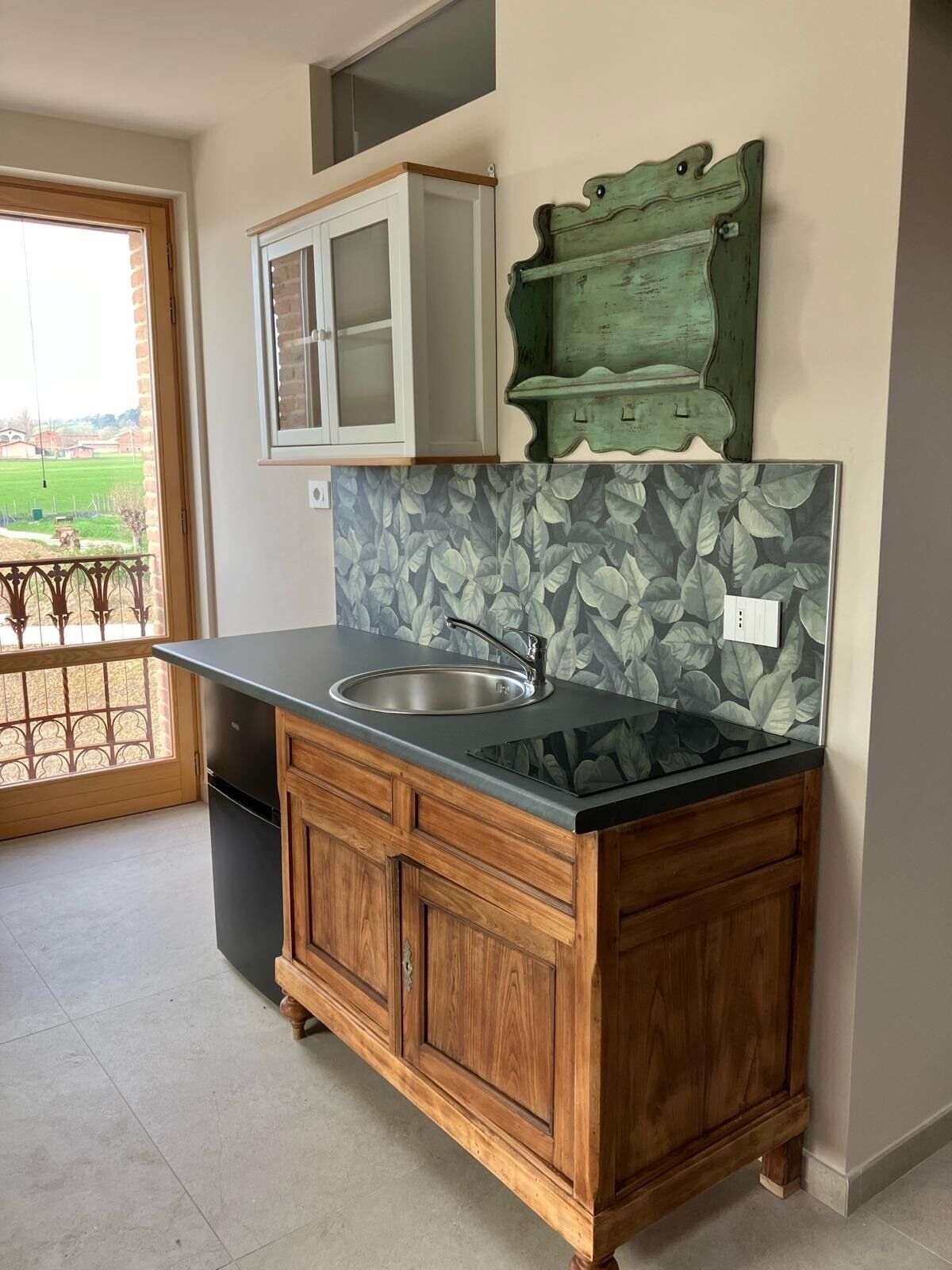 A kitchen with a wooden cabinet, a stainless steel sink, and a backsplash with leaf patterns.