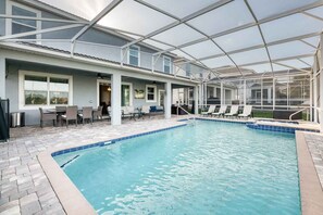 An indoor swimming pool with a covered patio area, lounge chairs, and a seating area with tables and chairs.