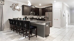 A modern kitchen with dark cabinets, a central island with bar stools, stainless steel appliances, and pendant lighting. - NEW! Gamers Paradise, Sauna, Theater, Pool/Spa, ChampionsGate, 8 Bed Luxury Home (Four Corners)