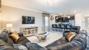 A modern living room with a black leather sofa, a coffee table, and a TV mounted on the wall. - NEW! Gamers Paradise, Sauna, Theater, Pool/Spa, ChampionsGate, 8 Bed Luxury Home (Four Corners)