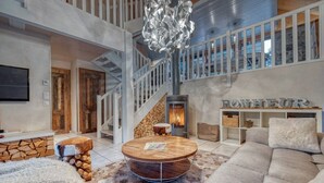 A spacious living area with a round coffee table, a fireplace, a staircase, and a large window. - Le Chalet des Eaux Piscine (Revel)