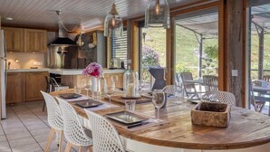 A modern kitchen with wooden cabinets, a stainless steel range hood, and a large island with white chairs. - Le Chalet des Eaux Piscine (Revel)