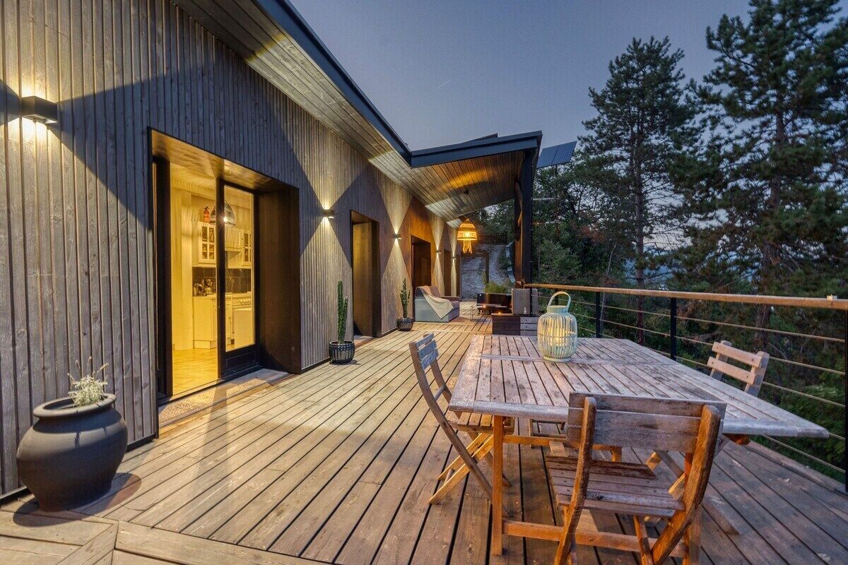 A wooden deck with a table and chairs, overlooking a mountainous landscape.