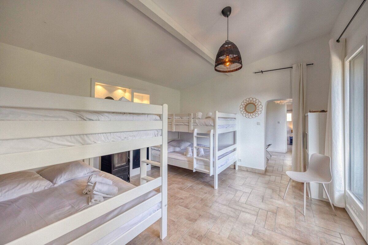 A room with bunk beds, a hanging light fixture, and a chair near a window.