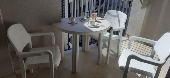 A small round table with two white plastic chairs, a white cup, and a glass pitcher on a balcony with a white railing.