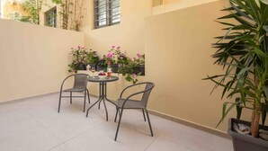 A small patio area with two chairs and a table, surrounded by potted plants and a window. - Yard Studio by Corfuescapes  (Corfu)
