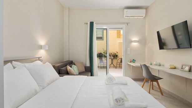 A hotel room with a large bed, a desk, a chair, a TV, and a sliding glass door leading to a balcony. - Yard Studio by Corfuescapes  (Corfu)