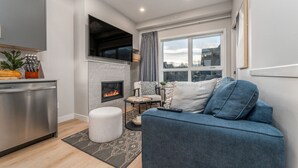 A modern living room with a fireplace, a sofa, a dining area, and a kitchen. - Skyview Retreat - Pool, Hot Tub &  Parking (Canmore)