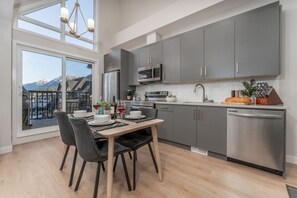 A modern kitchen with grey cabinets, stainless steel appliances, and a dining area with a table and chairs. - Skyview Retreat - Pool, Hot Tub &  Parking (Canmore)