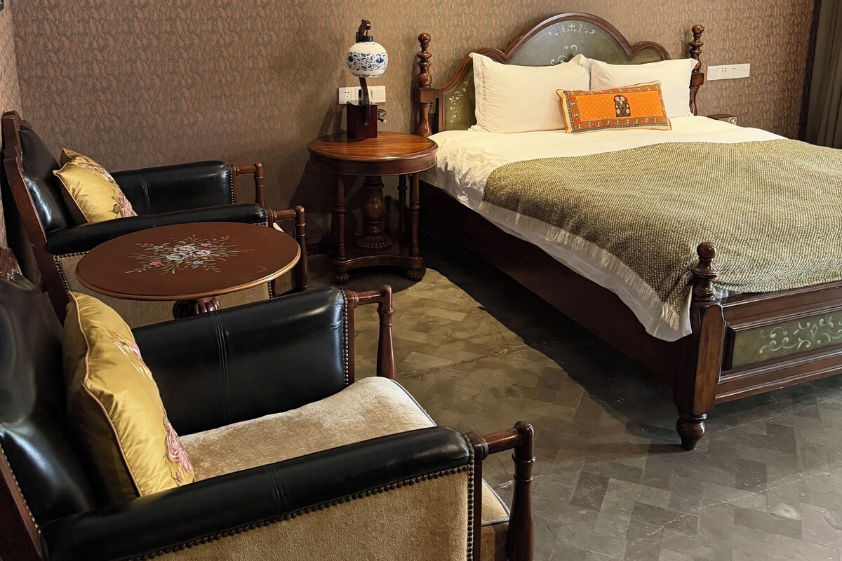 Une chambre d’hôtel avec un lit, une table ronde en bois, deux chaises et une petite table avec une lampe.