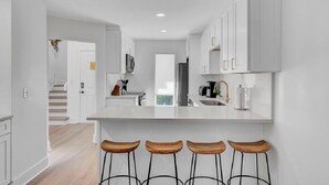 A modern kitchen with white cabinetry, a central island with stools, and a view to a balcony. - Award-Winning Resort Amenities | Racquet Club Villa 22 (Isle Of Palms)