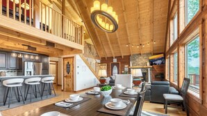 A spacious dining area with a long table set for a meal, a kitchen with modern appliances, and a cozy seating area with a fireplace. - A Mtn Frame of Mind- Mountain View, Hot Tub, Game Room, Pet Friendly (Seven Devil's)