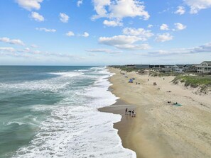 Ein Strand mit sandigem Ufer, Wellen im Ozean und eine Reihe von Häusern entlang der Küste.