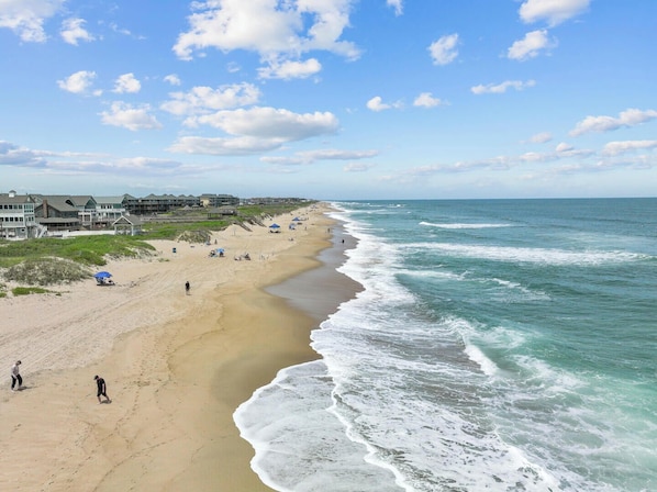 Une plage avec un rivage sablonneux, des vagues et des bâtiments en arrière-plan.