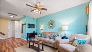 A living room with a ceiling fan, a sofa, a coffee table, and a television.