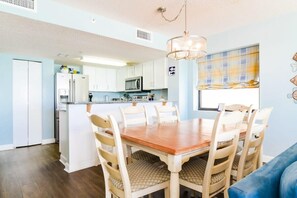 Une cuisine compacte avec des meubles blancs, un îlot central et un coin repas comprenant une table et des chaises en bois.