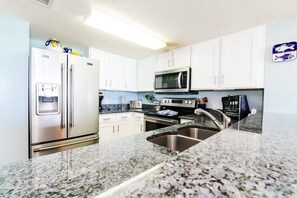 A kitchen with white cabinets, stainless steel appliances, a granite countertop, and a stainless steel sink.