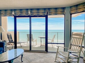 A balcony with a view of the ocean, furnished with chairs and a table.