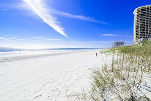 Une plage avec un ciel dégagé, un rivage sablonneux et un bâtiment situé sur la droite.