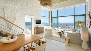 Uma sala de estar ampla com uma mesa de jantar de madeira, sofás brancos e uma grande janela com vista para o mar.