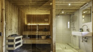 A sauna with wooden walls and a glass door, a sink, and a mirror in a bathroom.