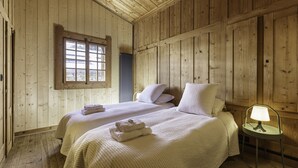A wooden cabin bedroom with two beds, a window, and a nightstand with a lamp.